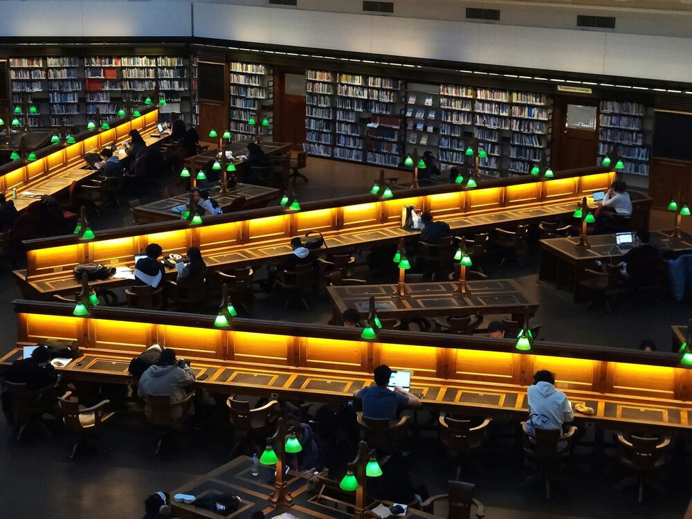 Lernende in einer Bibliothek an beleuchteten Tischen